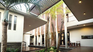 Un pati interior modern amb sòl de fusta, palmeres i una zona de seients coberta.