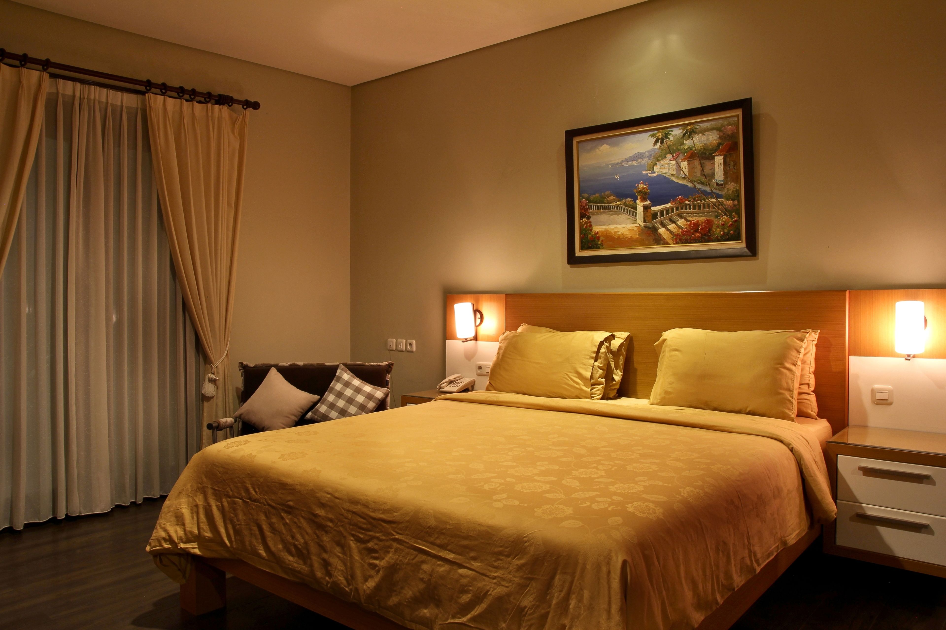 Una habitación de hotel con una cama grande, una mesita de noche, un cuadro en la pared y una ventana con cortinas.