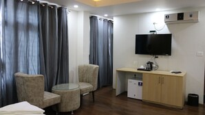 A hotel room with a bed, two armchairs, a small round table, a TV, a desk with a computer, and a mini-fridge. - Hotel Mustang Holiday Inn (Kathmandu)