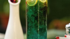 A tall glass with a green beverage, garnished with lemon slices and an orange straw. - Hotel Mustang Holiday Inn (Kathmandu)