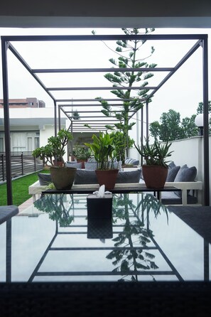 A modern outdoor seating area with a glass table, potted plants, and a bench. - Hotel Mustang Holiday Inn (Kathmandu)