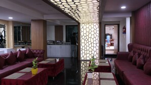 A modern hotel lobby with red upholstered sofas, a central decorative panel, and a kitchen area in the background. - Hotel Mustang Holiday Inn (Kathmandu)