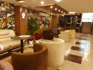 Un vestíbulo moderno con un sofá, sillones, una mesa de centro y una planta grande.