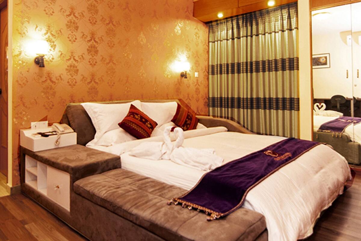 Una habitación de hotel con una cama grande, un banco de madera, una mesita de noche y un espejo.
