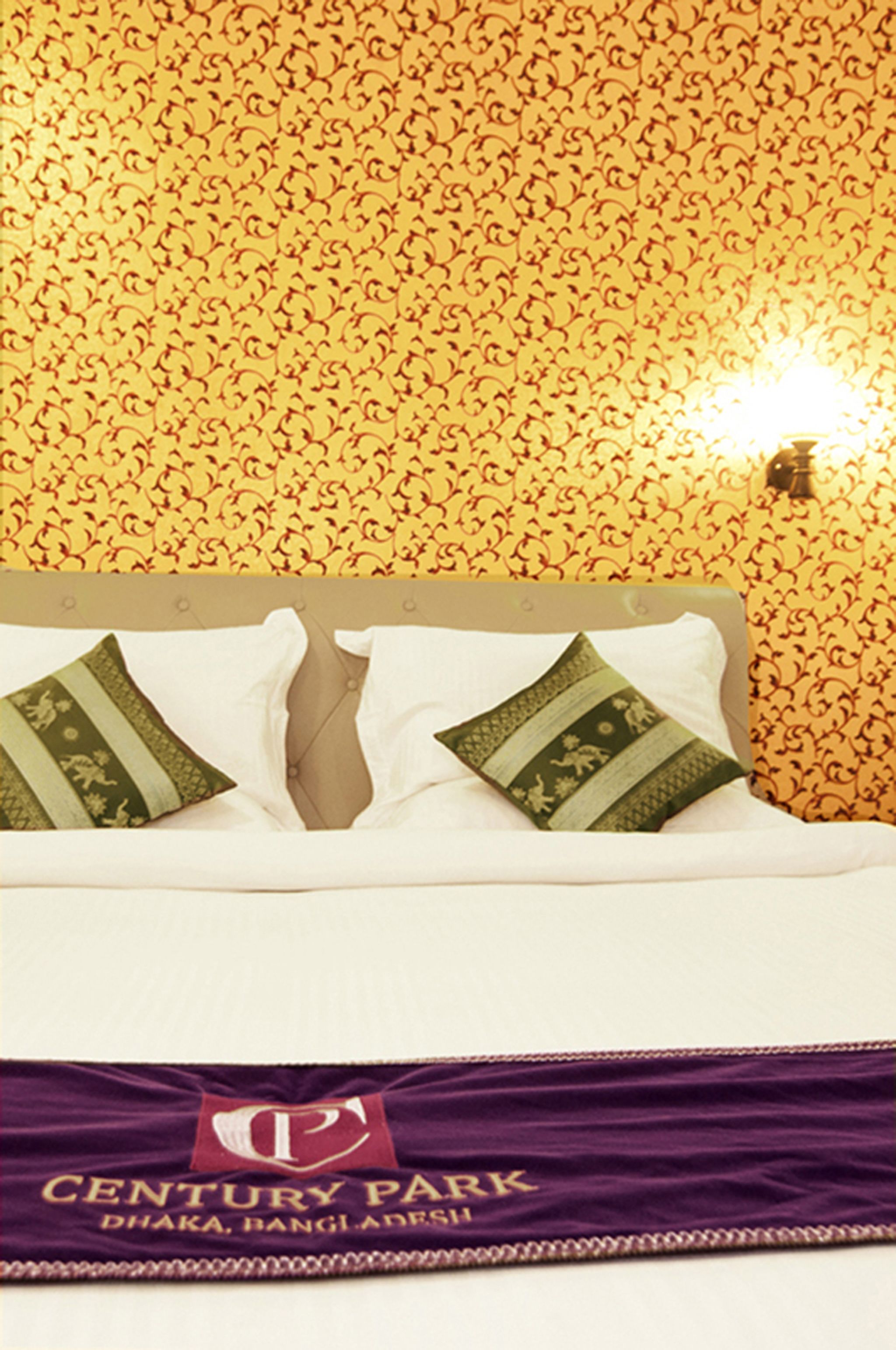A bed with a headboard, two decorative pillows, and a purple bedspread with a logo.