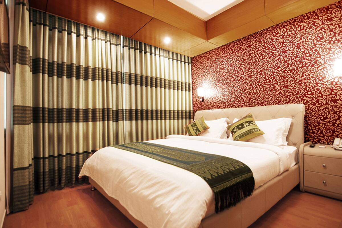 Una habitación de hotel con una cama grande, una mesita de noche, un papel tapiz decorativo y cortinas.