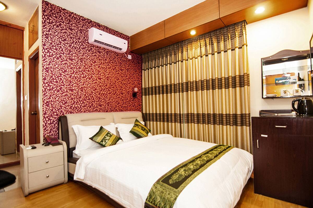 Una habitación de hotel con cama, mesita de noche, cómoda y un equipo de aire acondicionado en la pared.