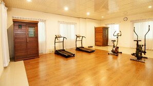 A spacious room with a wooden floor, a door, and exercise equipment including treadmills and an elliptical. - Century Park Residence (Dhaka)