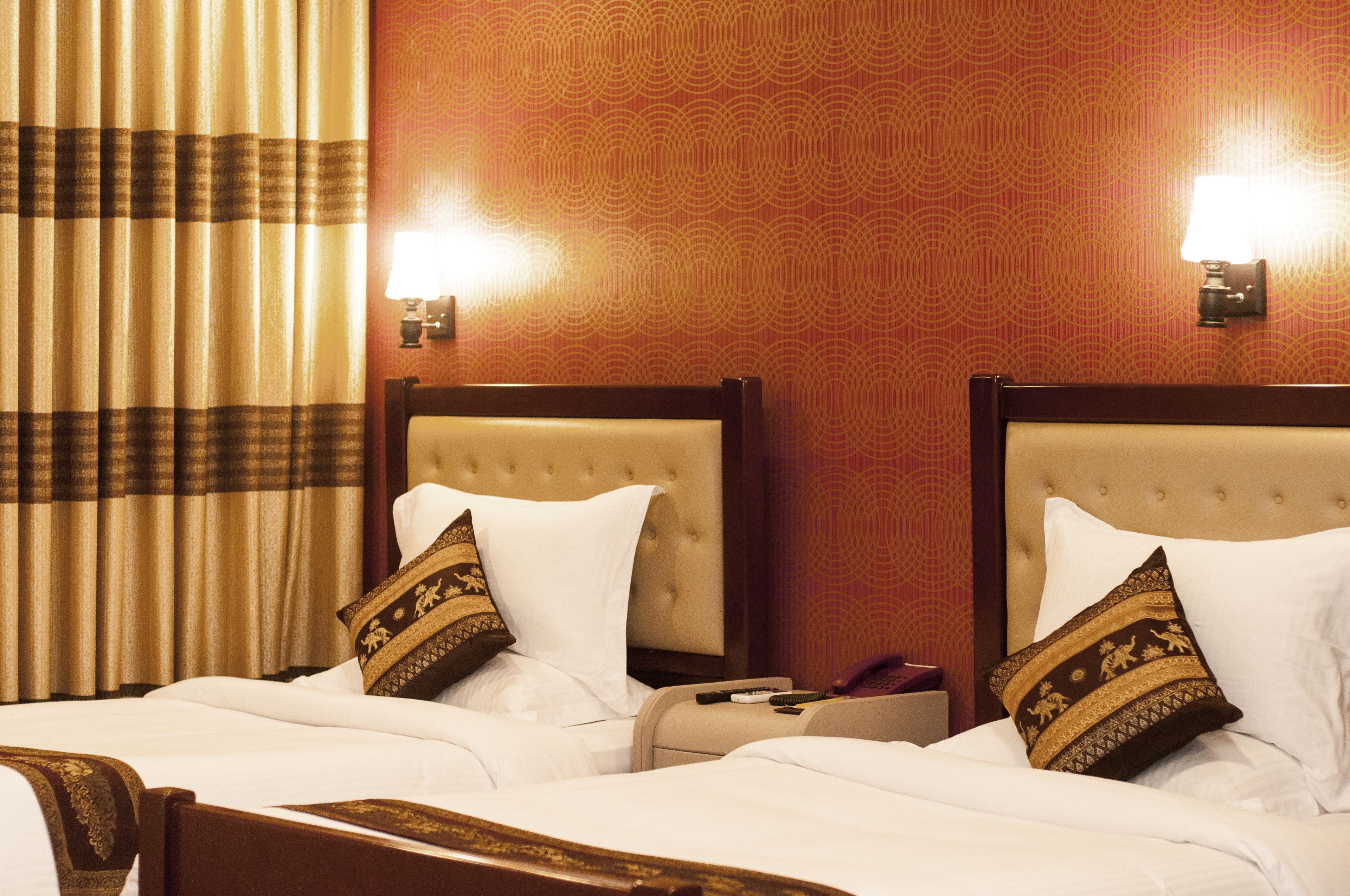 A hotel room with two beds, each with a headboard, a lamp, and a pillow with a patterned design.