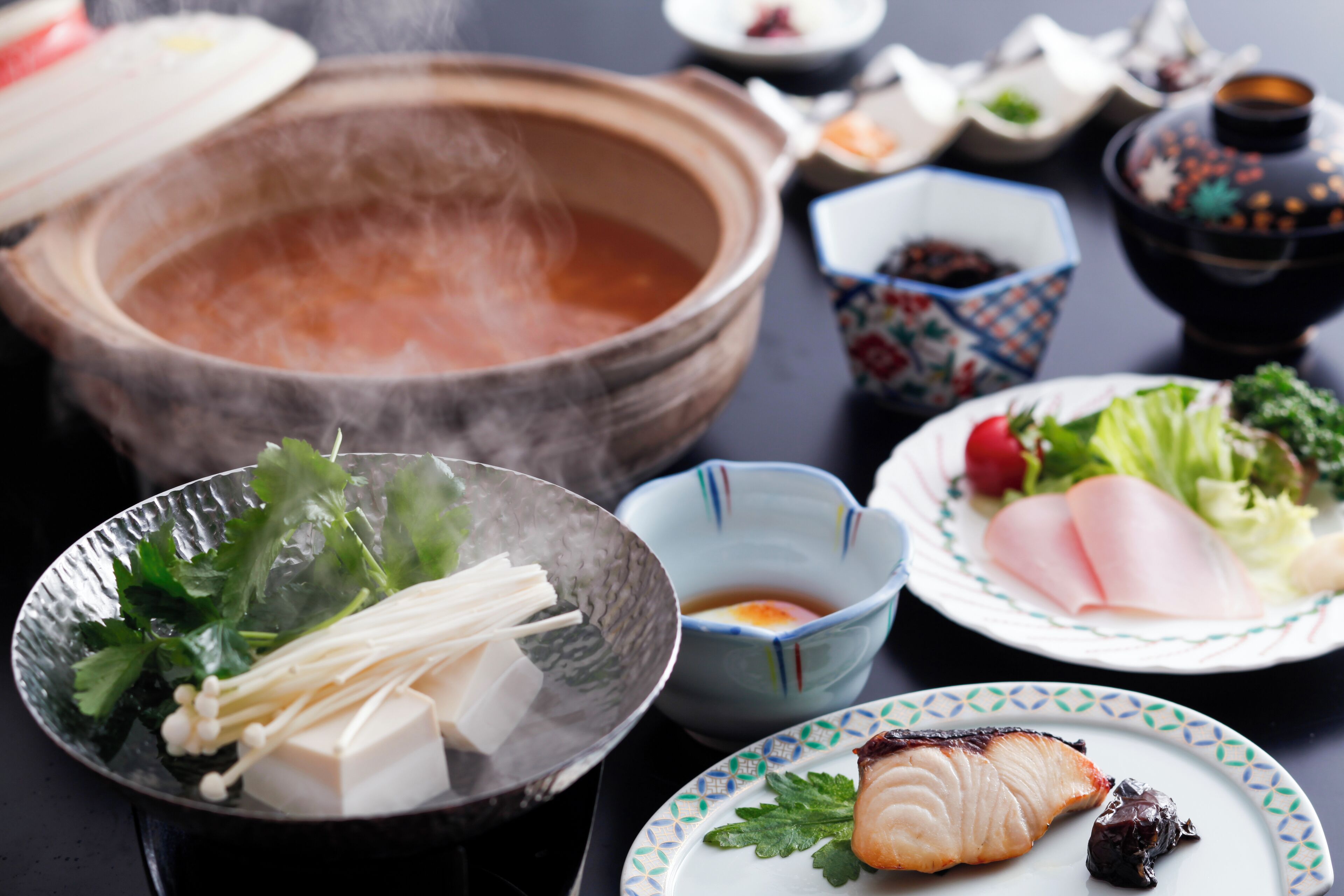A table with various dishes including a bowl of soup, a plate with sashimi, and a bowl of tofu.