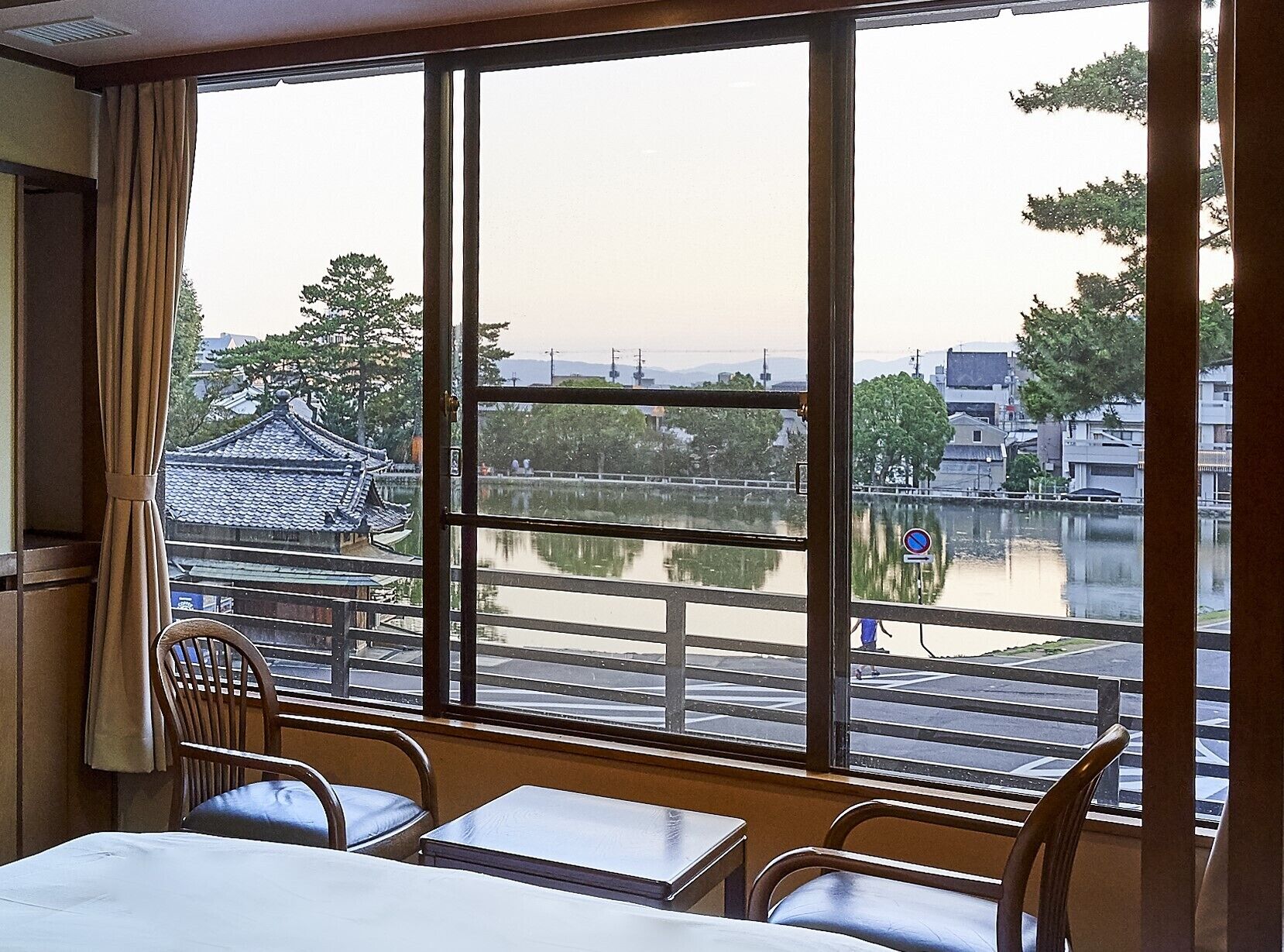 A room with a large window offering a view of a traditional building across a body of water, a table, and two chairs.