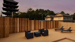Una terraza en la azotea con cerca de madera, sillas de descanso y un pabellón al fondo.