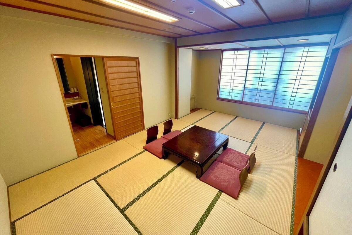 Una habitación con esteras de tatami, una puerta corredera, una mesa de tatami y vistas al exterior a través de una ventana.