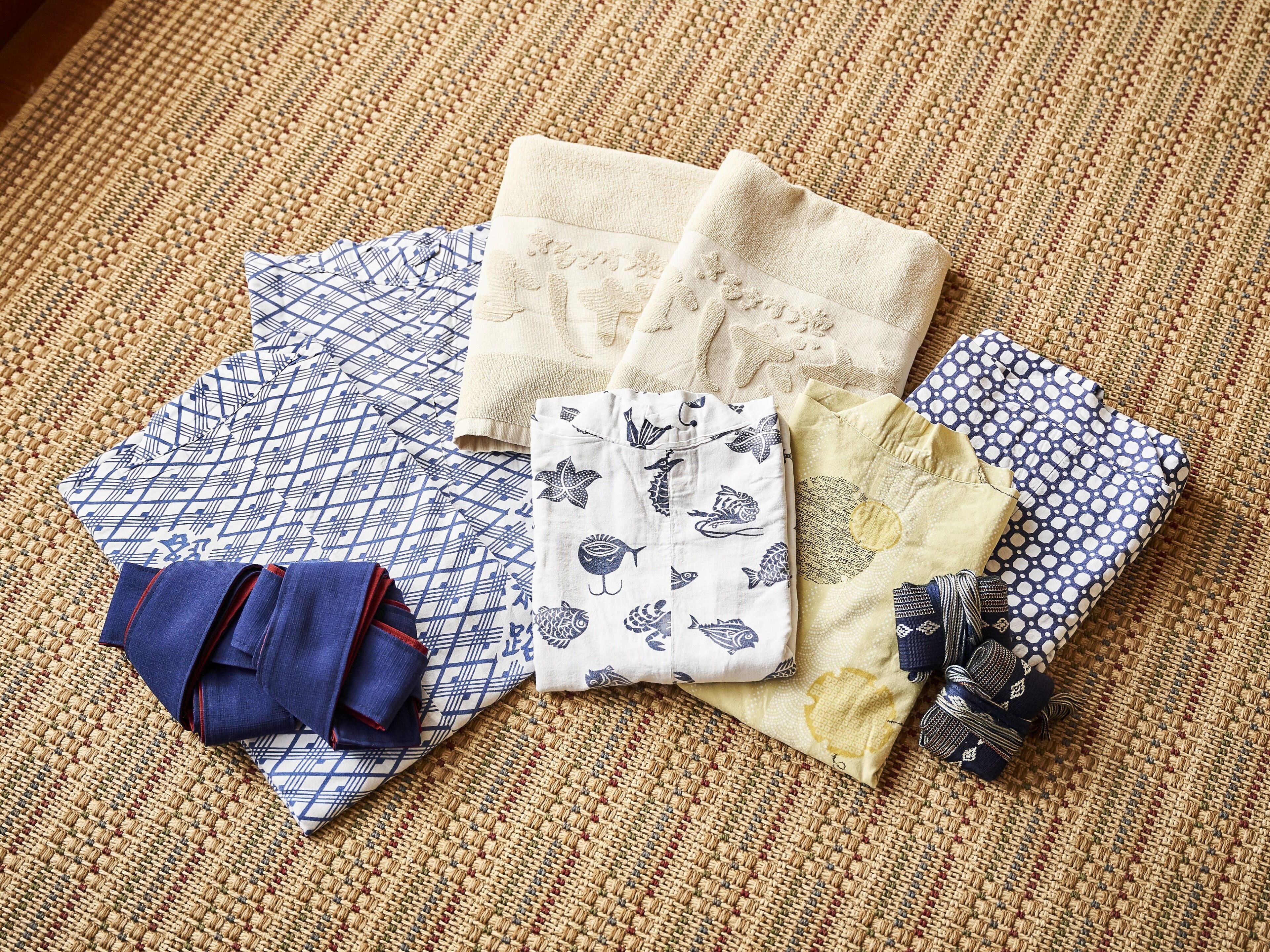 A variety of folded textiles and fabrics on a woven mat.