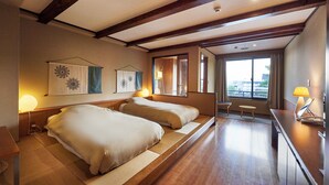 Habitación de hotel con dos camas, una mesita, una lámpara, ventana con vistas y vigas de madera en el techo.