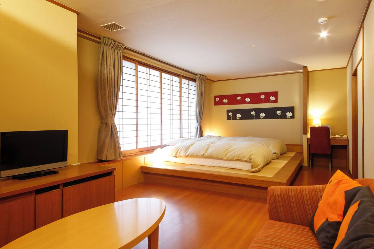 Una habitación de hotel con una cama, televisión, escritorio y ventana con cortinas.