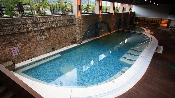 An indoor swimming pool with a stone wall and a view of greenery outside. - Hoya Hot Springs Resort & Spa (Taimali)