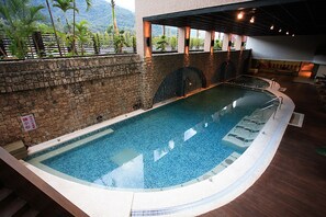 An indoor swimming pool with a stone wall and a view of greenery outside. - Hoya Hot Springs Resort & Spa (Taimali)