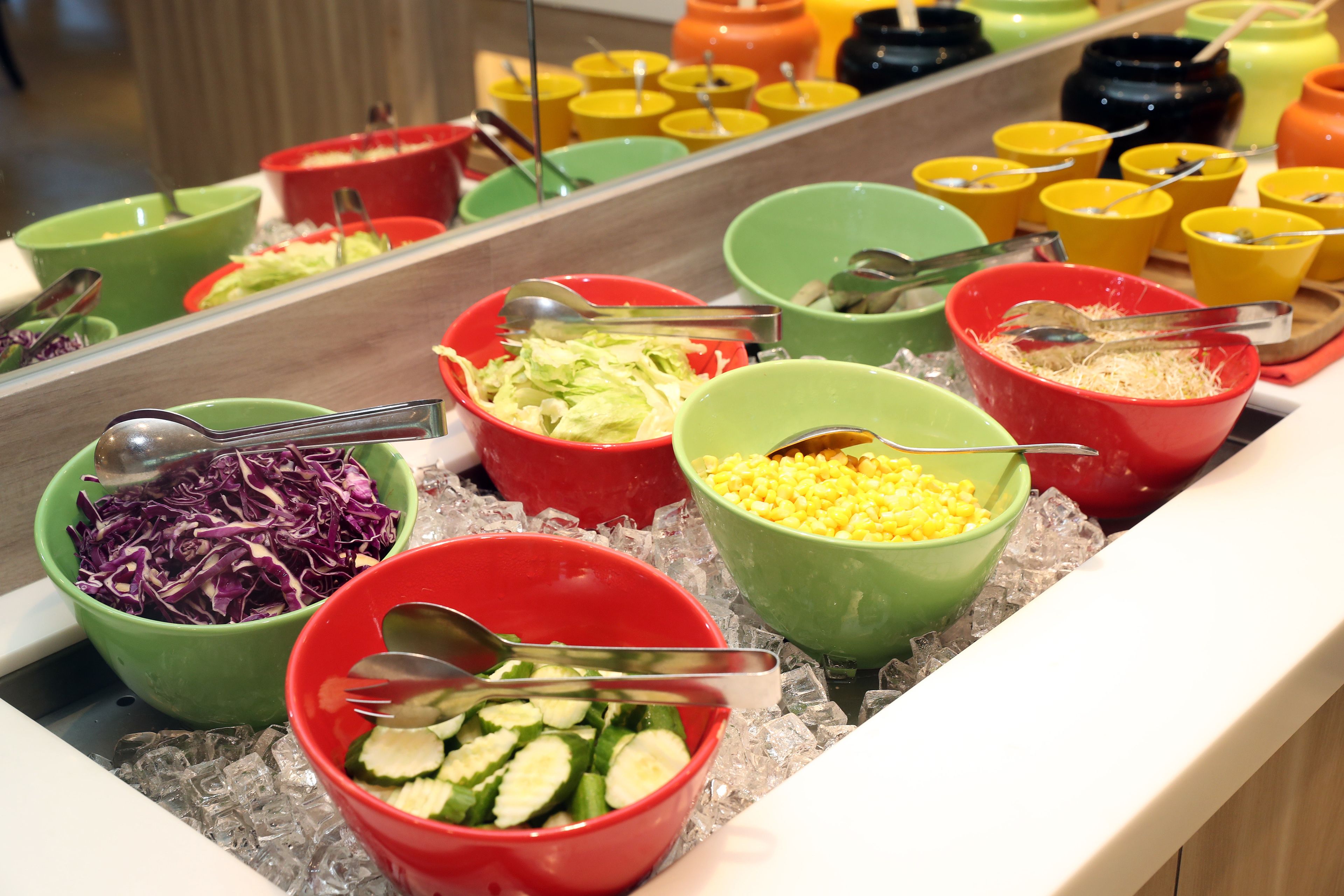 A buffet with various food items in colorful bowls on ice.