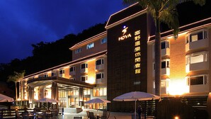 A hotel with a covered outdoor area, multiple dining tables with umbrellas, and a sign with Chinese characters. - Hoya Hot Springs Resort & Spa (Taimali)