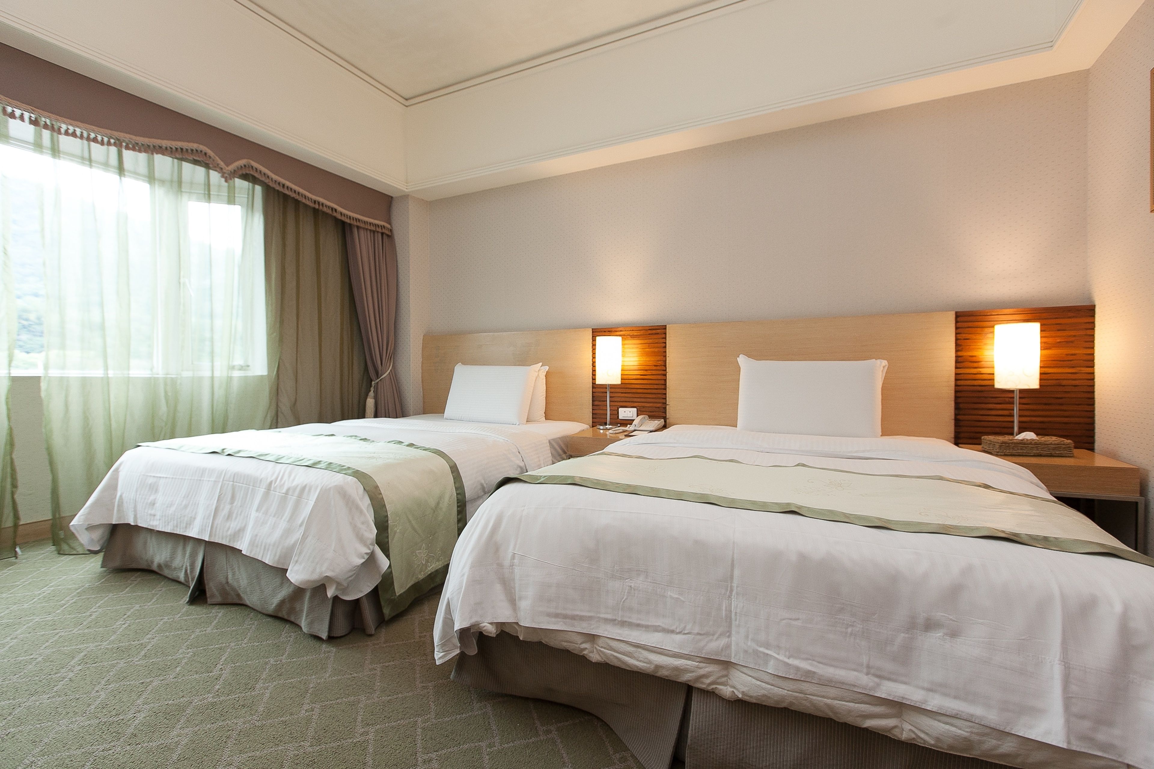 A hotel room with two beds, a large window with curtains, and bedside lamps.
