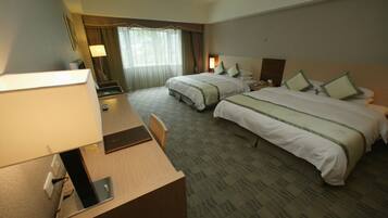 A hotel room with two beds, a desk, a lamp, and a window with curtains.