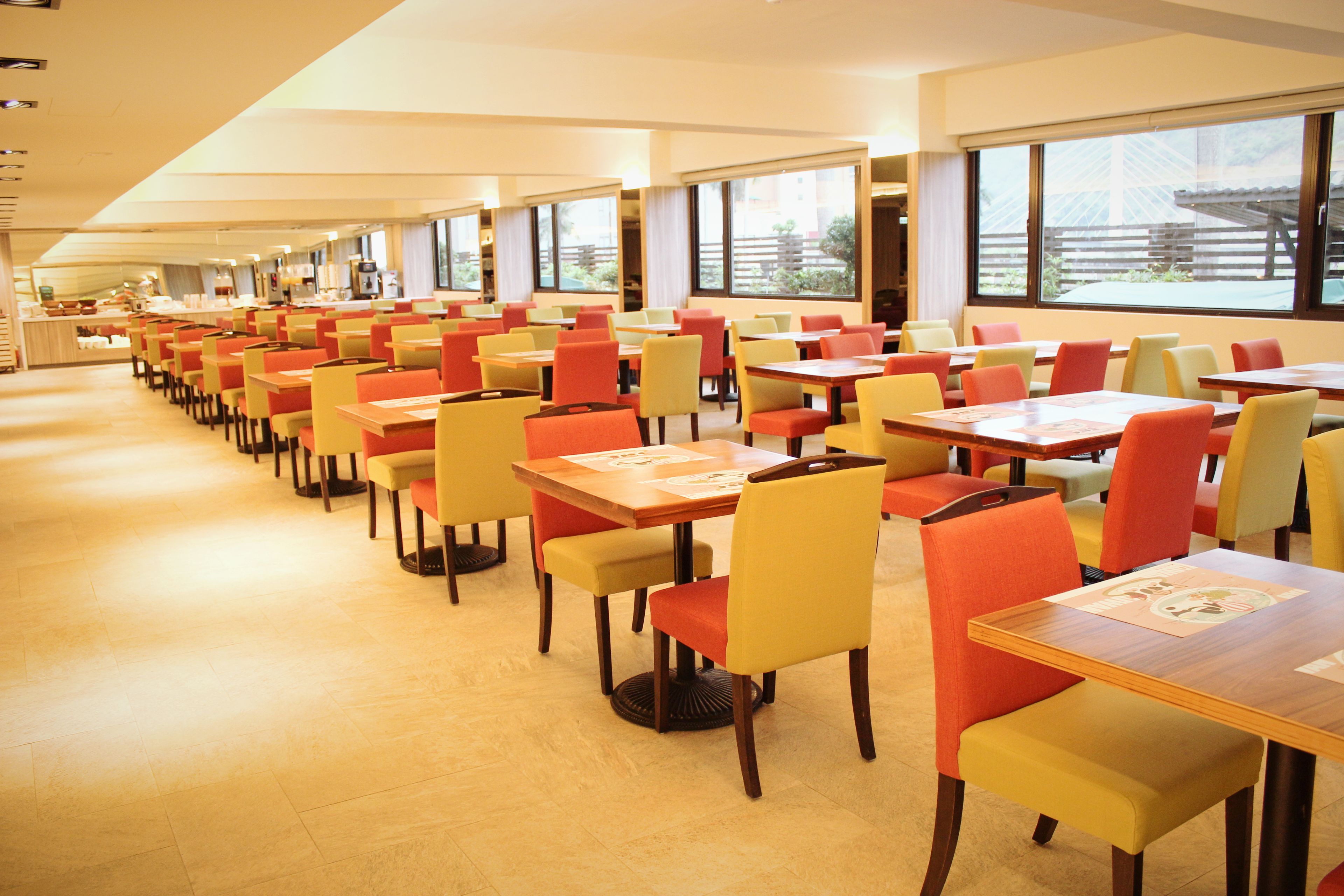 A spacious dining area with multiple tables and chairs, large windows providing natural light, and a clean, modern interior design.