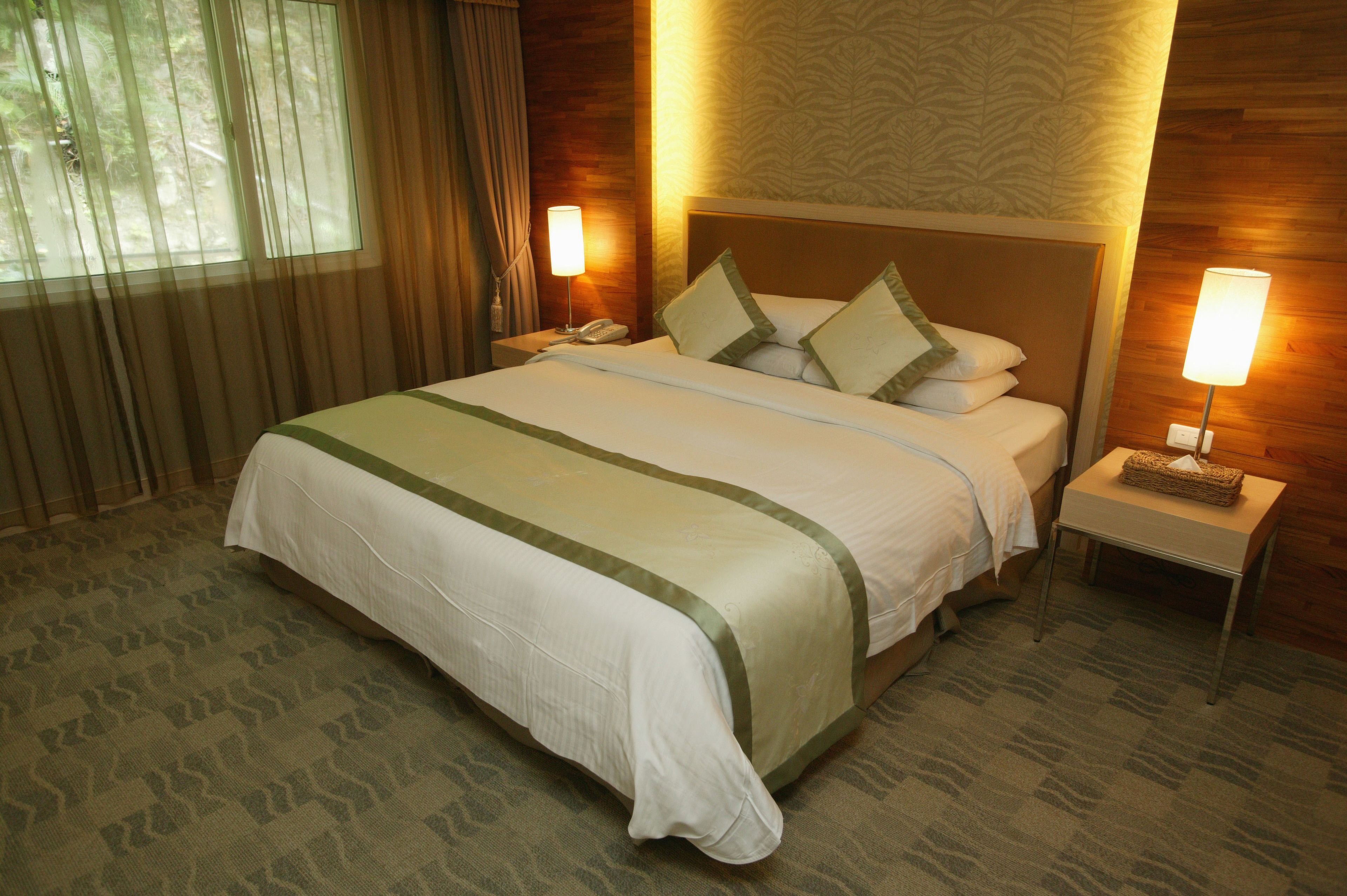 Una habitación de hotel con una cama grande, dos mesitas de noche y una lámpara en cada una.