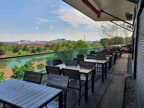 An outdoor seating area with tables and chairs, overlooking a body of water and greenery.