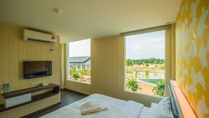 Habitación de hotel con cama, televisión, escritorio y ventana que ofrece vistas a un edificio y zonas verdes.