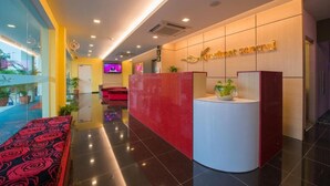 Zona de recepción de hotel con diseño moderno, que incluye un mostrador de recepción, una pantalla de televisión y un área de estar con un banco estampado.