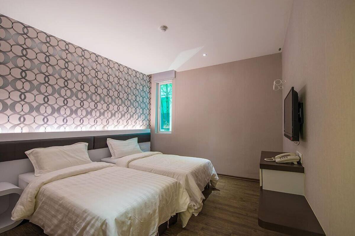 Habitación de hotel con dos camas, un escritorio pequeño con teléfono, televisión montada en la pared y un papel tapiz decorado.