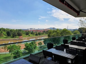 A balcony with a view of a river, trees, and distant buildings.