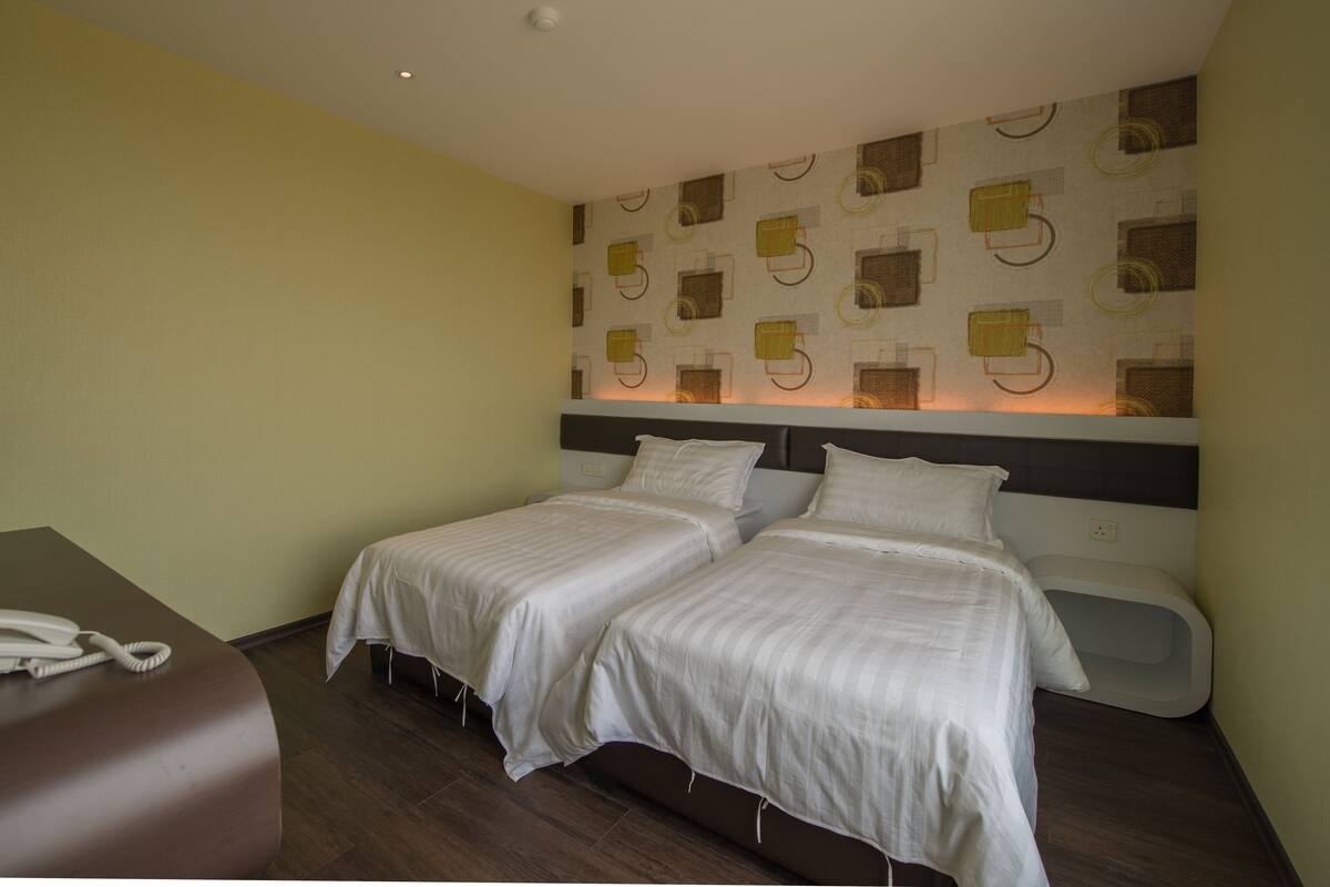 Una habitación de hotel con dos camas individuales, un escritorio y teléfono, y una pared con diseño.