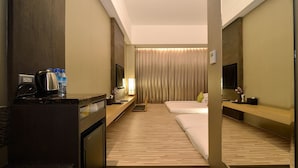 A hotel room with a wooden floor, a bed, a desk with a kettle, a TV, and a curtain. - Hoya Resort Hotel Taitung (Taitung)