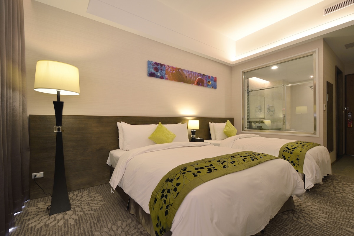 Une chambre d’hôtel avec deux lits, une table de chevet, une lampe, un tableau et un grand miroir.