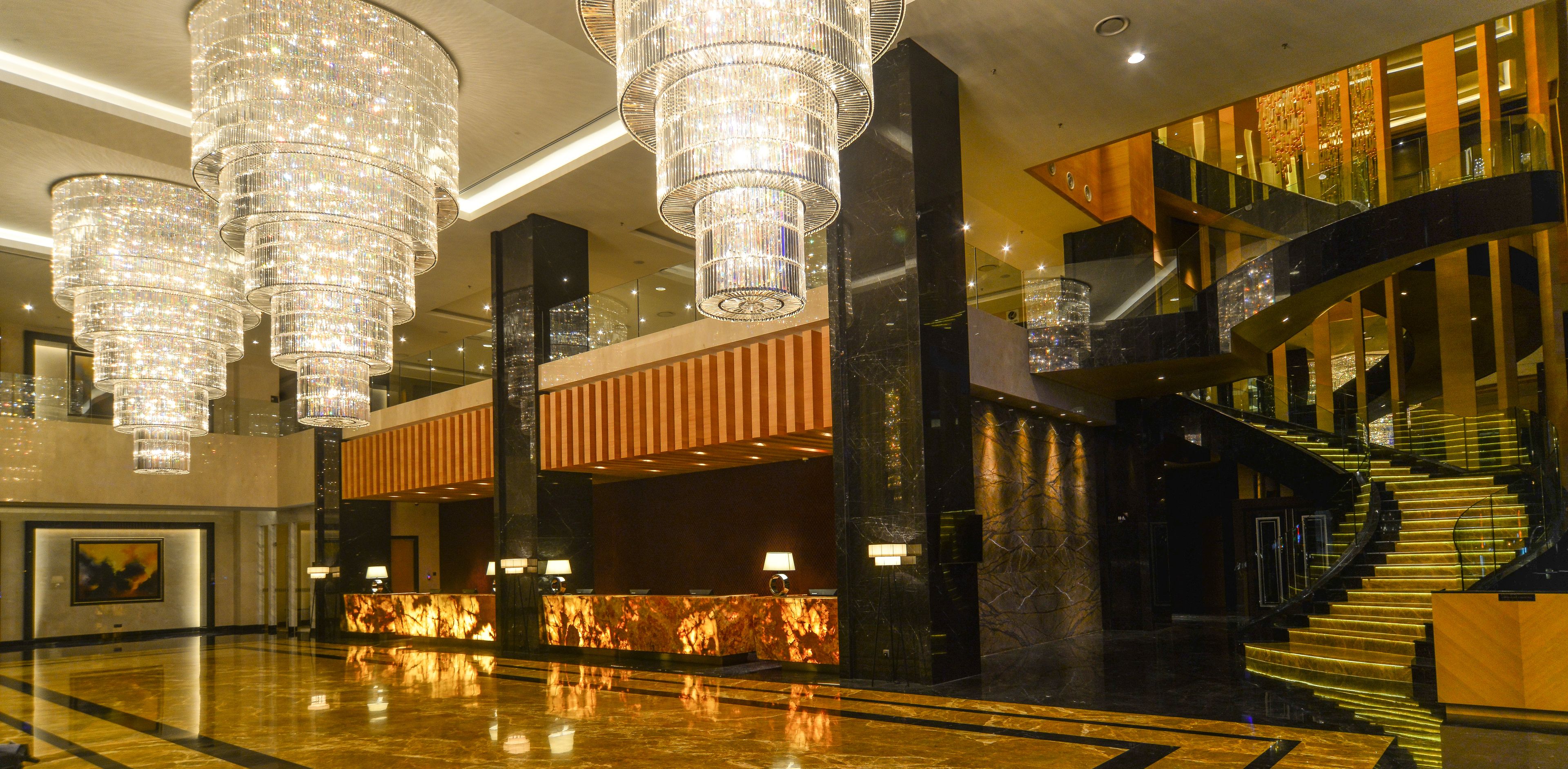 A luxurious lobby with multiple chandeliers, a grand staircase, and a reception desk.