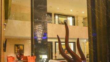 A lobby with a glass partition, a large abstract sculpture, and a seating area with orange chairs.