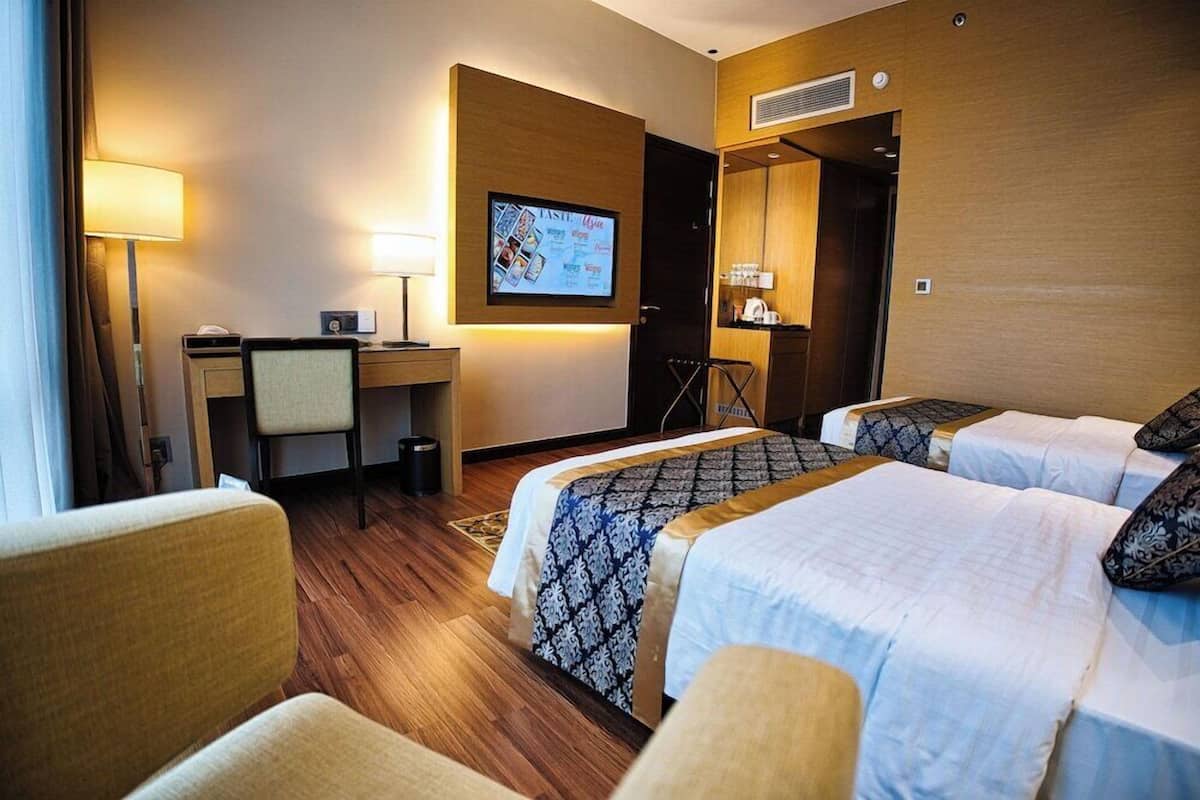 Une chambre d’hôtel avec deux lits, un bureau, une chaise et un écran de télévision affichant un menu.