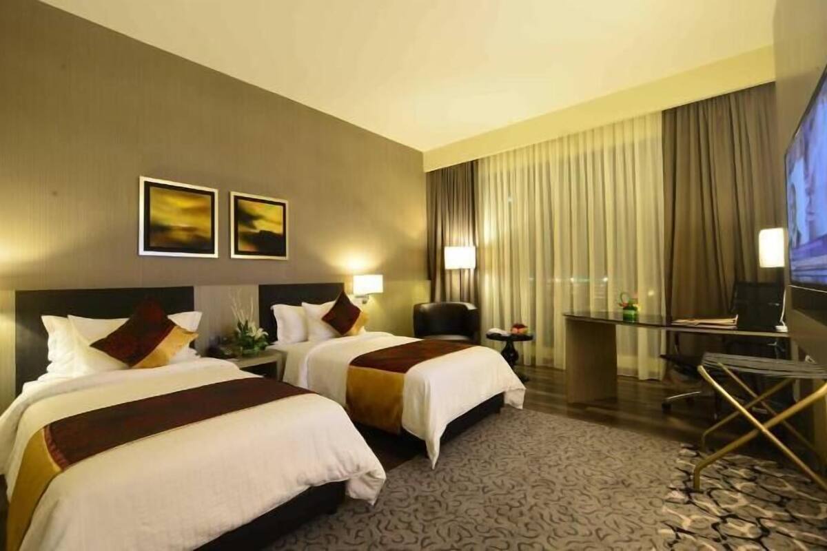 Une chambre d’hôtel avec deux lits, un bureau, une chaise, une télévision et une grande fenêtre avec des rideaux.