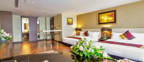 A hotel room with a bed, bedside tables, a desk, and a flower arrangement.