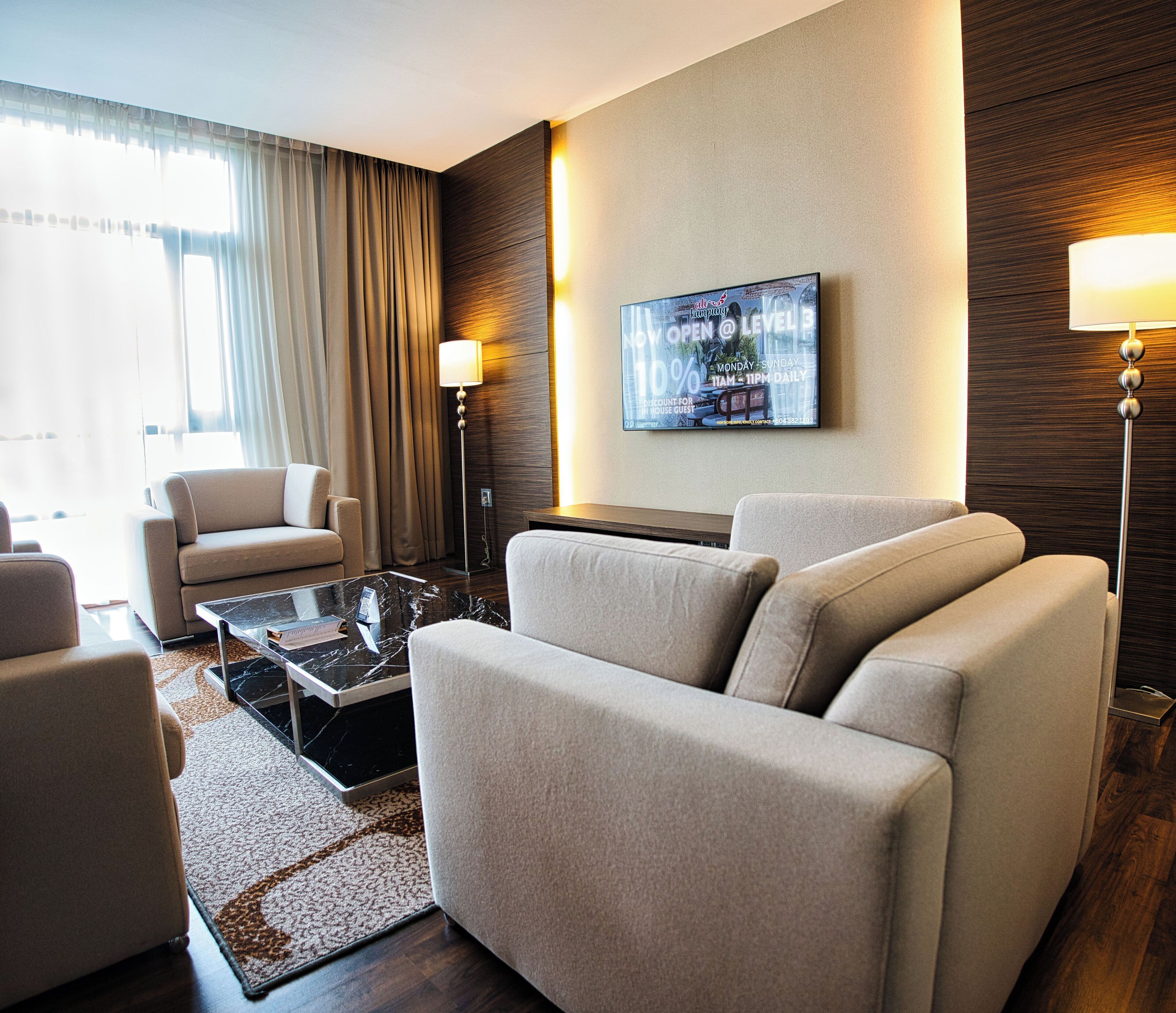 A modern hotel room with a sofa set, a coffee table, and a flat-screen TV mounted on the wall.