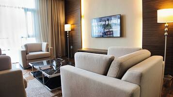 A modern hotel room with a sofa set, a coffee table, and a flat-screen TV mounted on the wall.