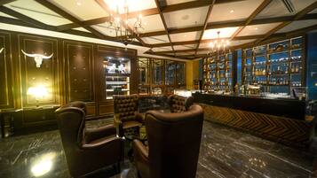 A bar area with leather chairs, a marble floor, and a wall of liquor bottles.