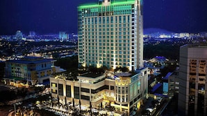 Ein hoch aufragendes Hotel mit modernem Design, dessen markanter oberer Bereich grün beleuchtet ist, umgeben von anderen Gebäuden und einer belebten Stadtlandschaft.