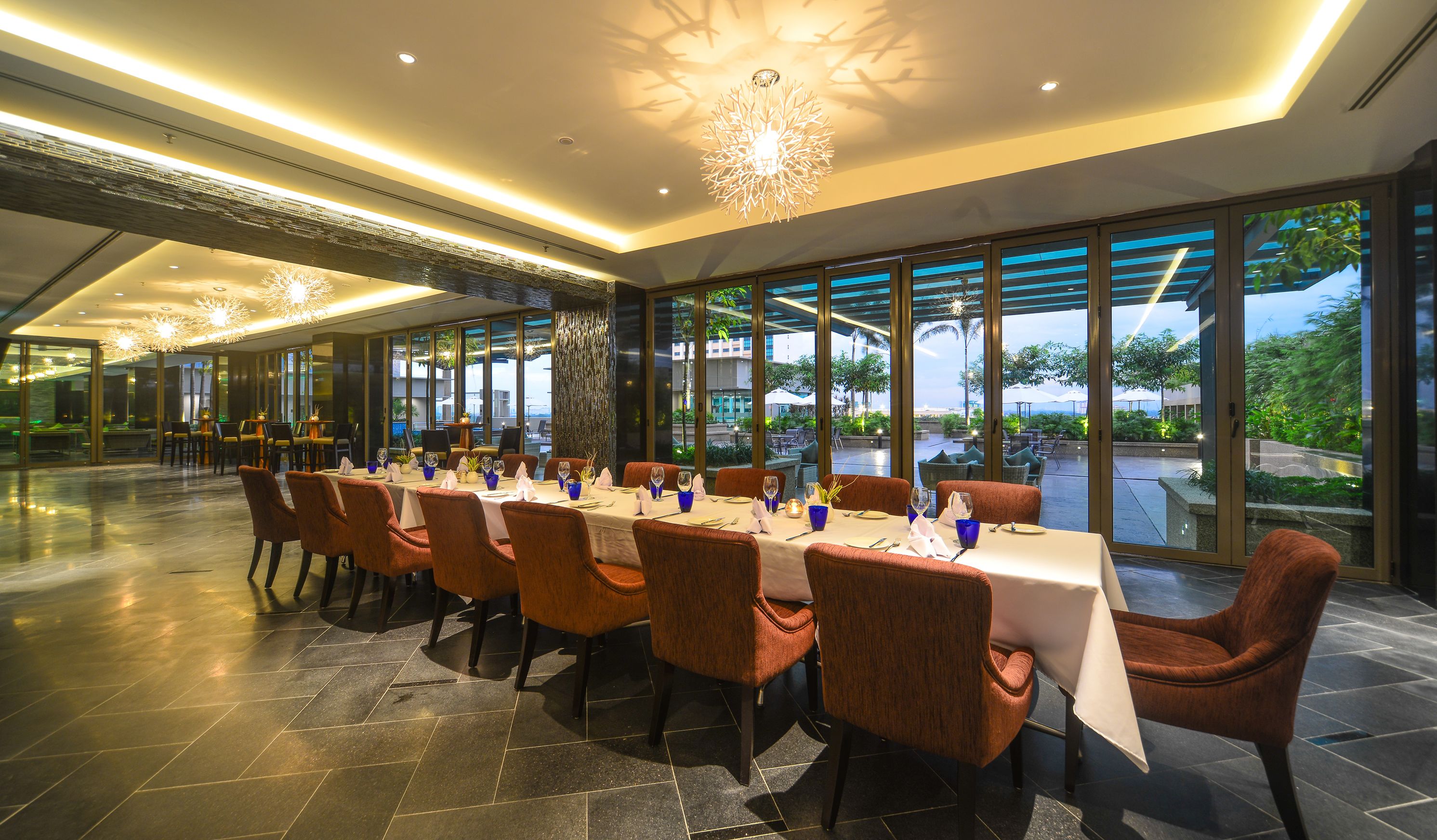 A dining area with tables set for six, large windows, and a modern chandelier.