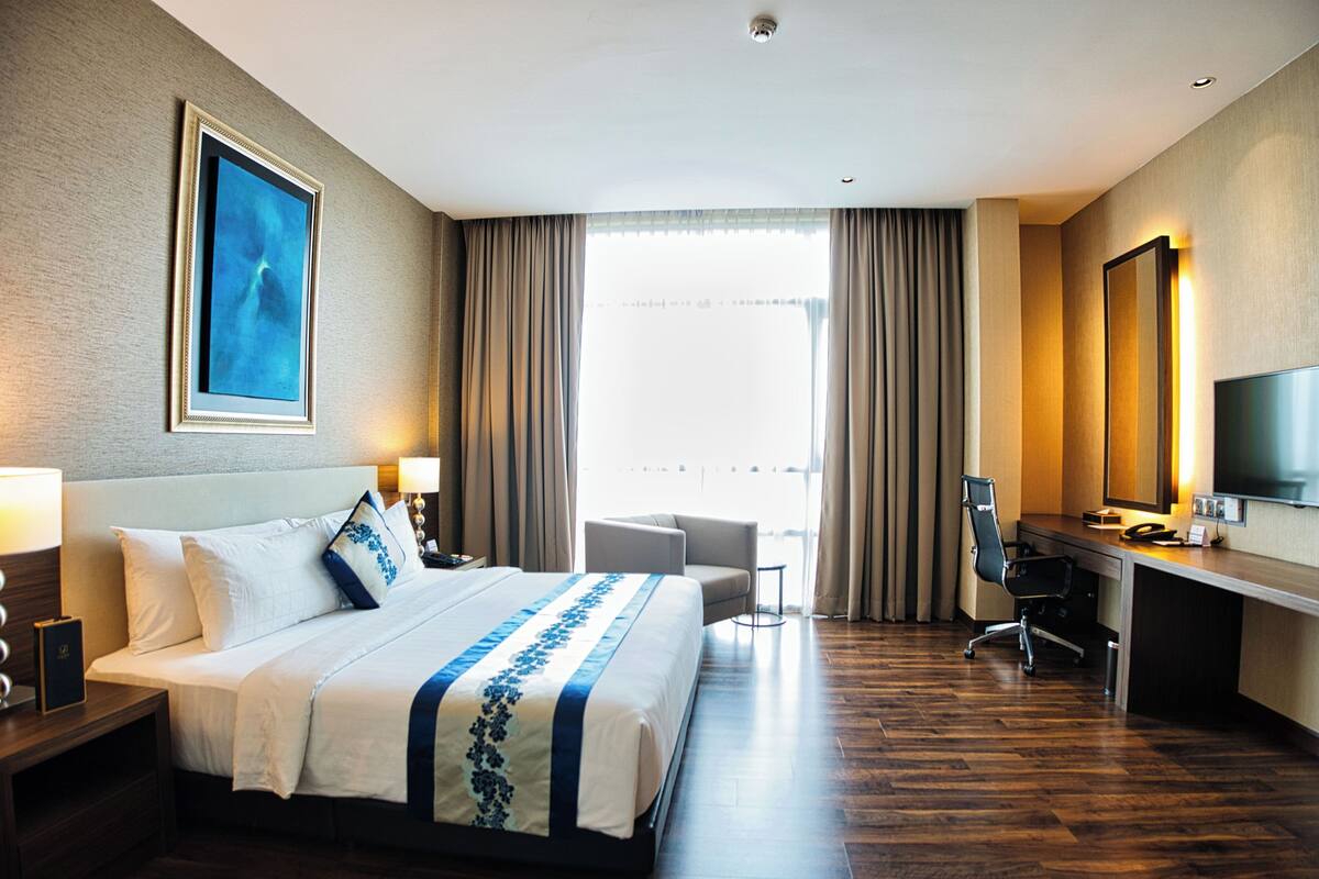 Une chambre d’hôtel avec un grand lit, un bureau, une chaise, une télévision et une fenêtre avec des rideaux.