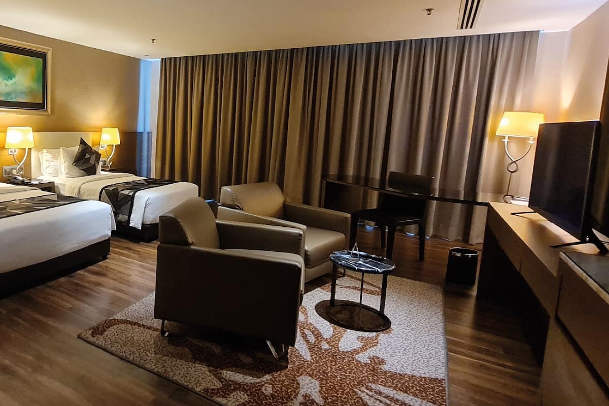 Une chambre d’hôtel avec un grand lit, deux tables de chevet avec des lampes, un canapé, une télévision et une grande fenêtre avec des rideaux.