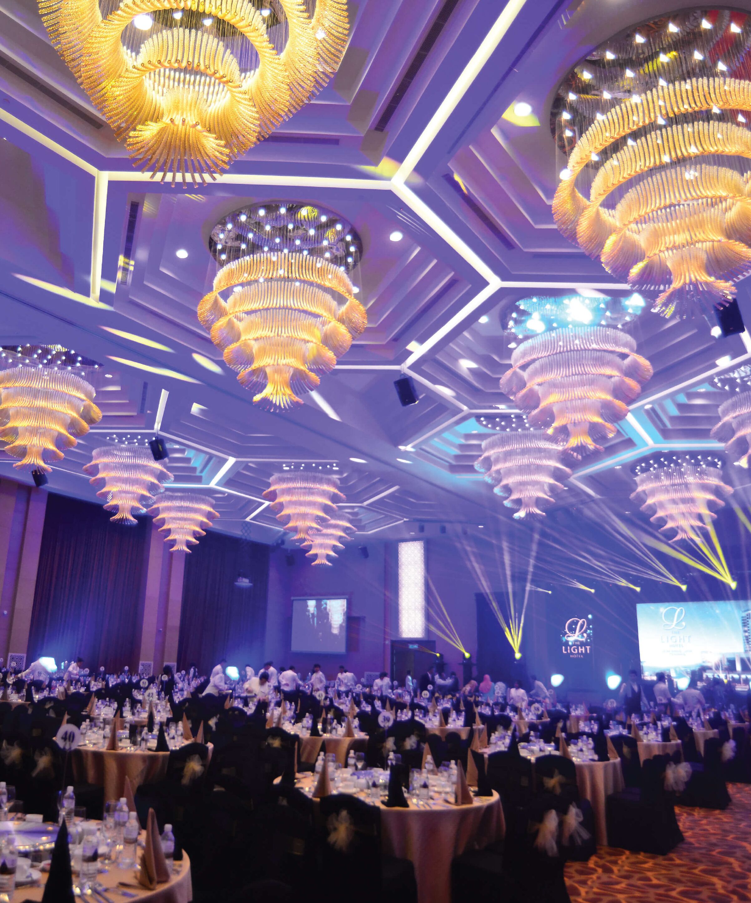 A large banquet hall with multiple round tables, each set with white tablecloths and black chairs.
