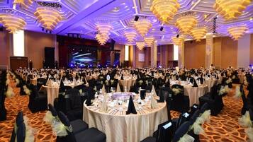 A banquet hall with round tables, black chairs, and chandeliers.